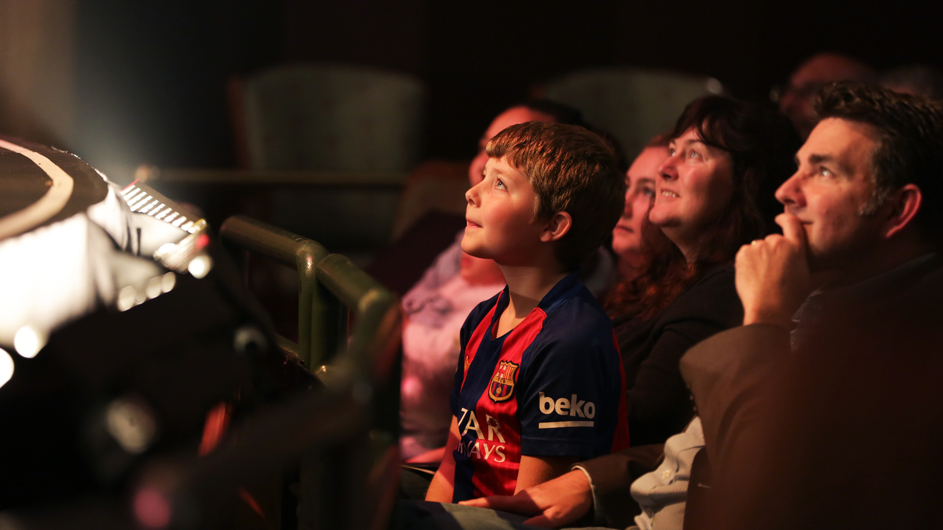 boy in soccer jersey sitting in theater leaning forward in his seat