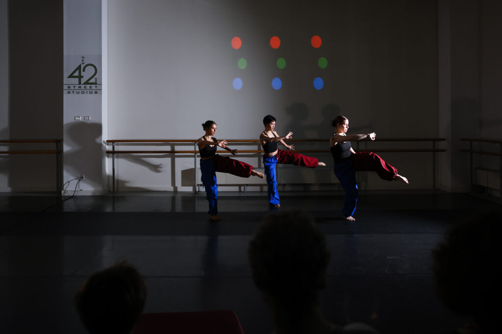 Three women performers wearing red and blue pants rehearsing in a New42 studio.