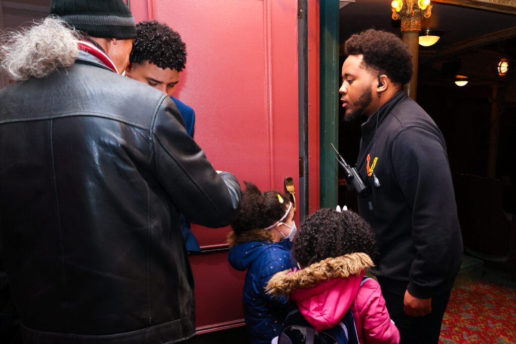 A youth corps member helping a family in the theater.