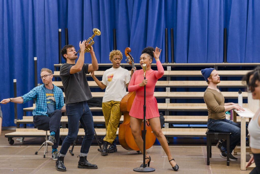 Trumpet player, base player and pianist flank singer at standing microphone