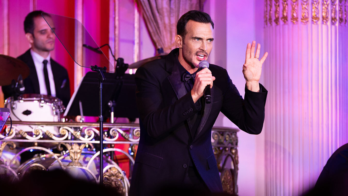 Cheyenne Jackson singing expressively into microphone on stage